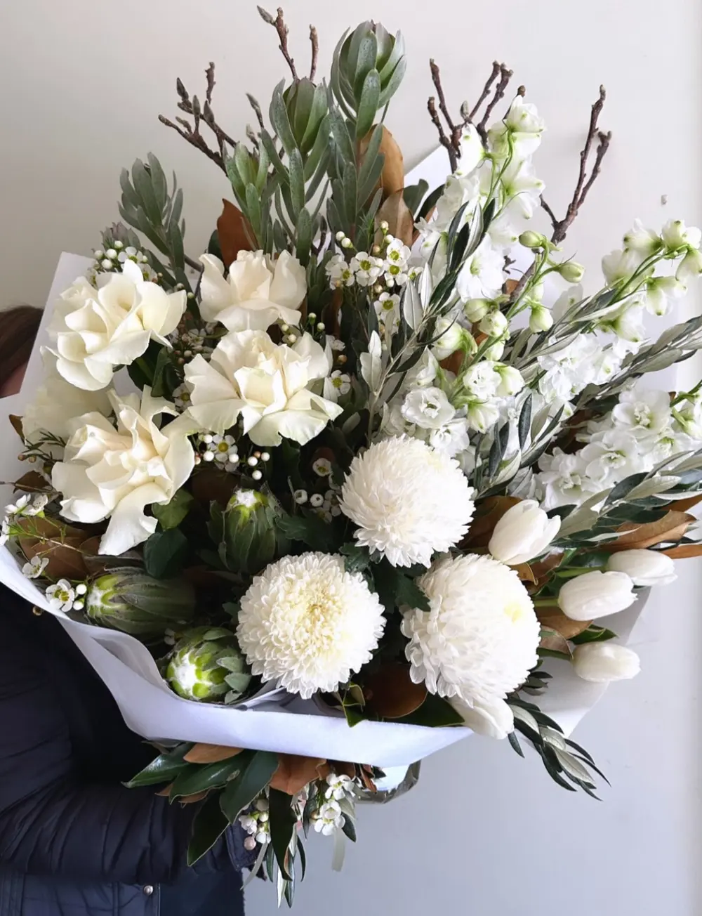 White bouquet of roses, chrysanthemums and silver foliage wrapped in white paper