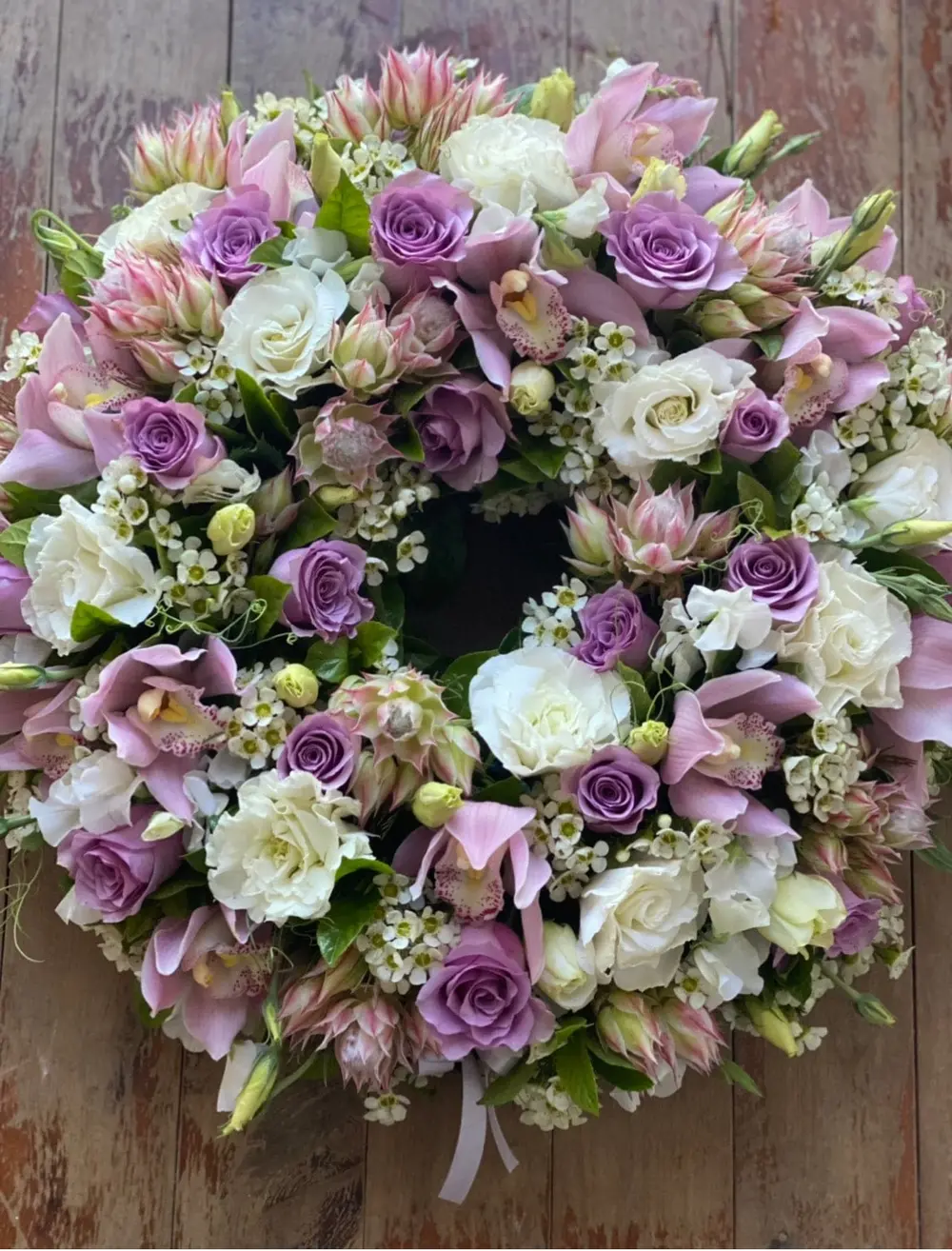 Sympathy wreath of lilac and white roses with soft pink blooms and waxflower
