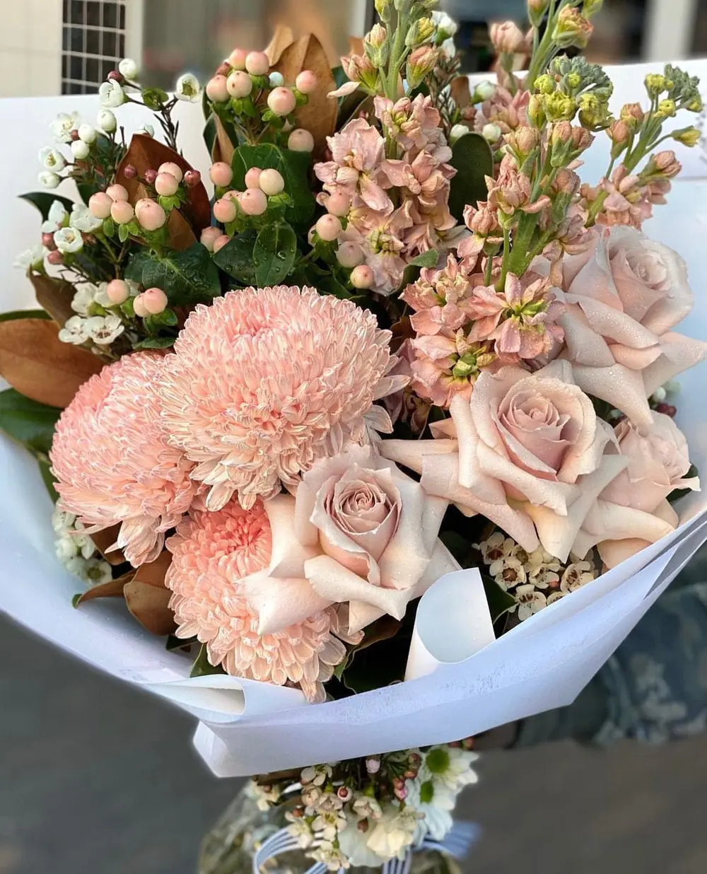 Soft pastel bouquet of peach chrysanthemums, dusty pink roses and stock wrapped in white paper